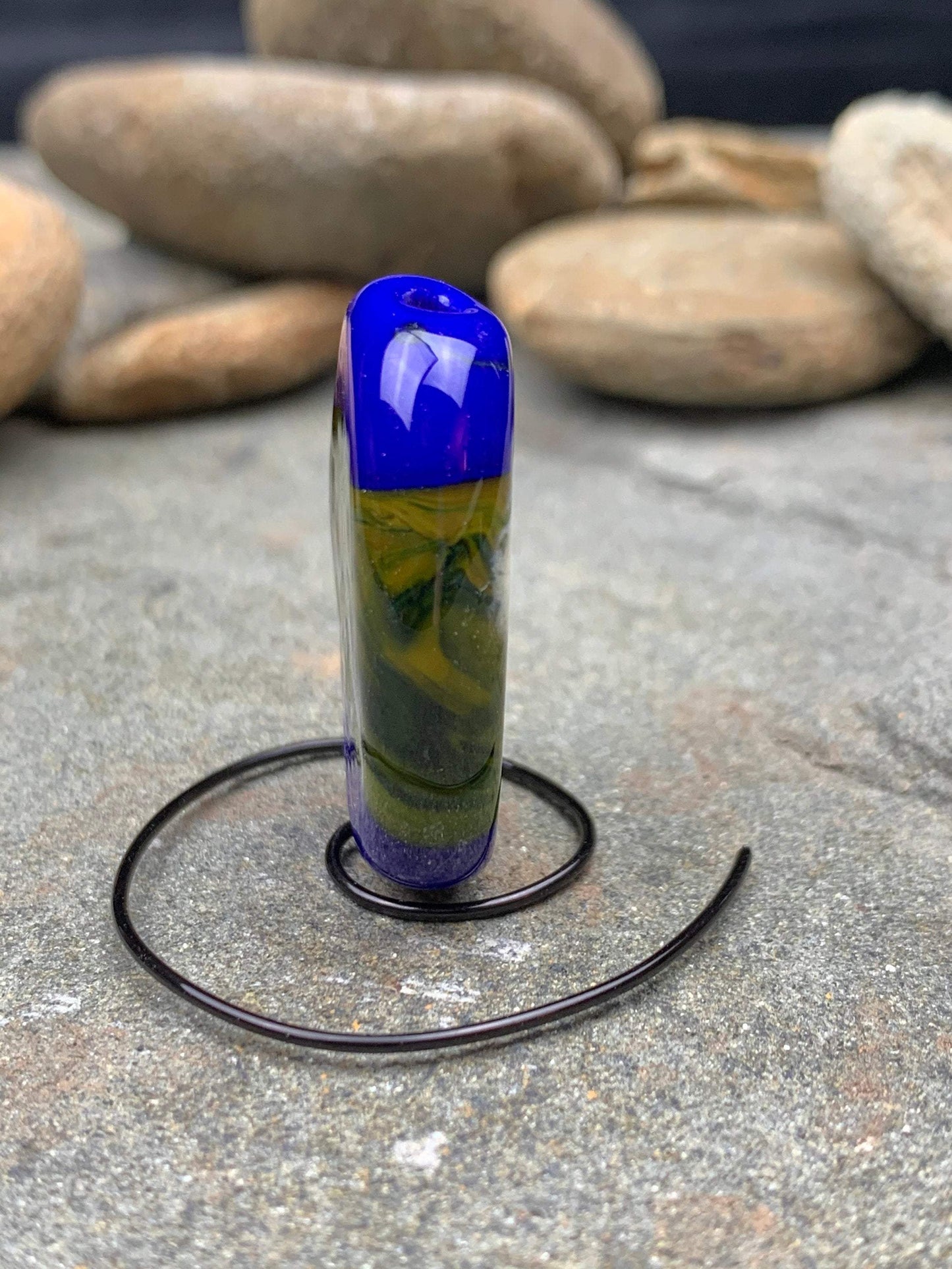a handmade lampworked glass bead with blue and white dots on a green background