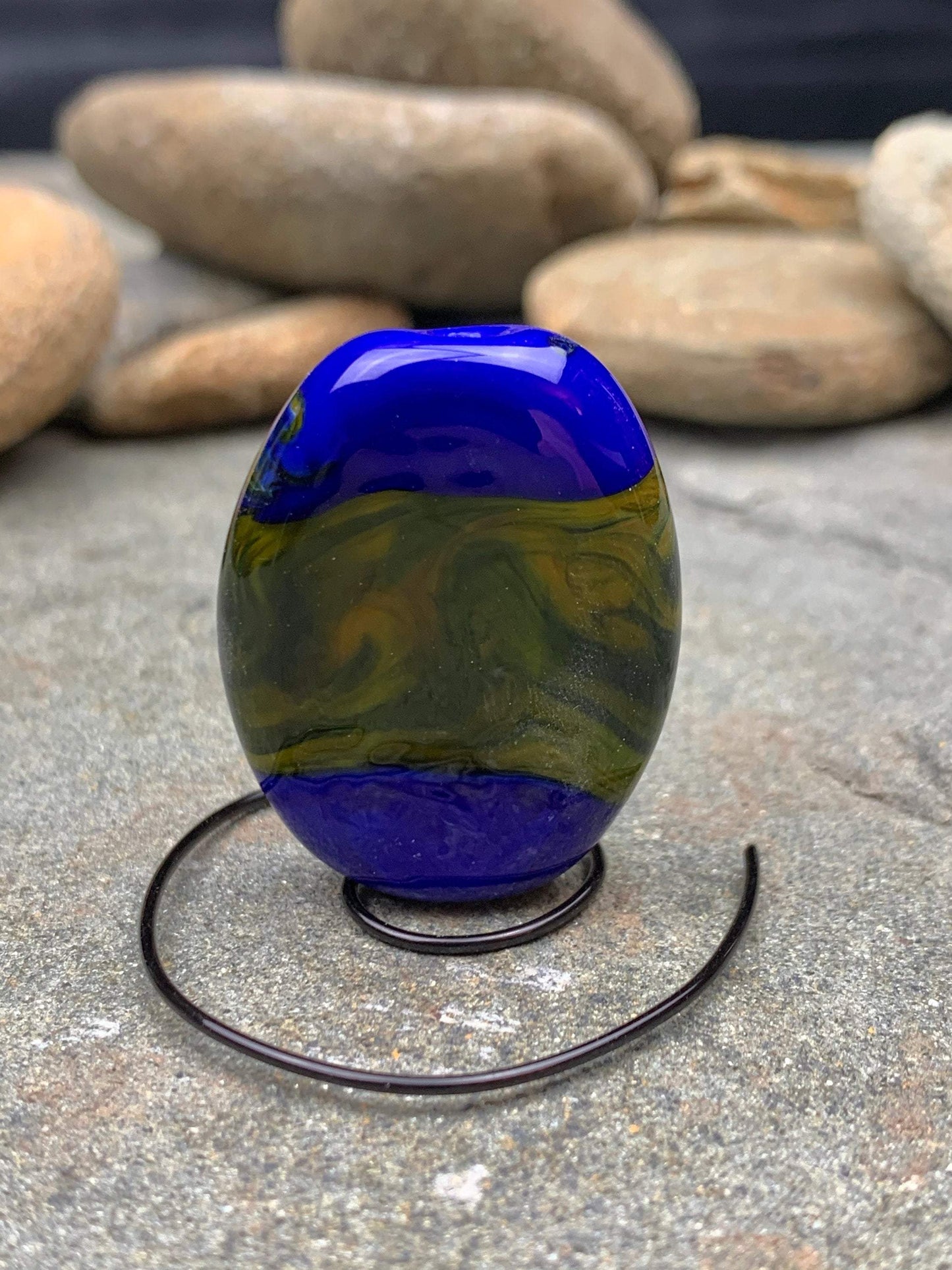 a handmade lampworked glass bead with blue and white dots on a green background