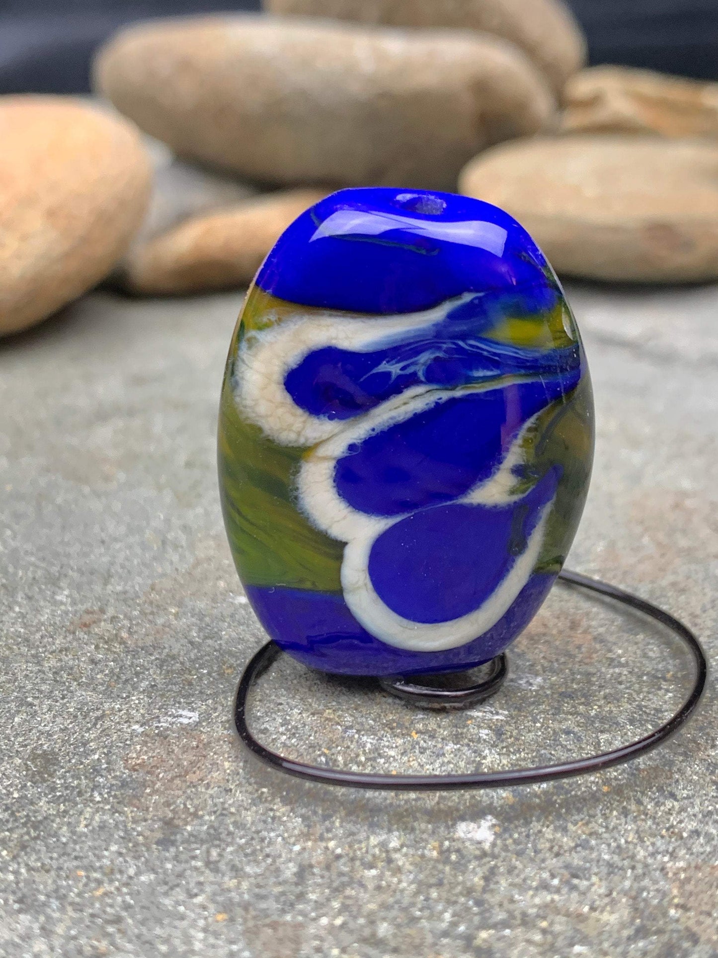 a handmade lampworked glass bead with blue and white dots on a green background