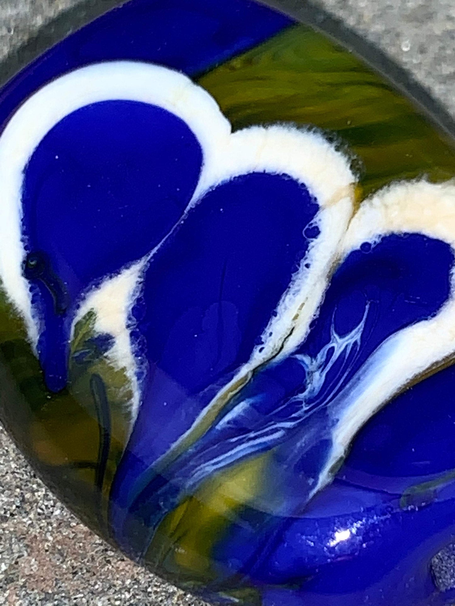 a handmade lampworked glass bead with blue and white dots on a green background