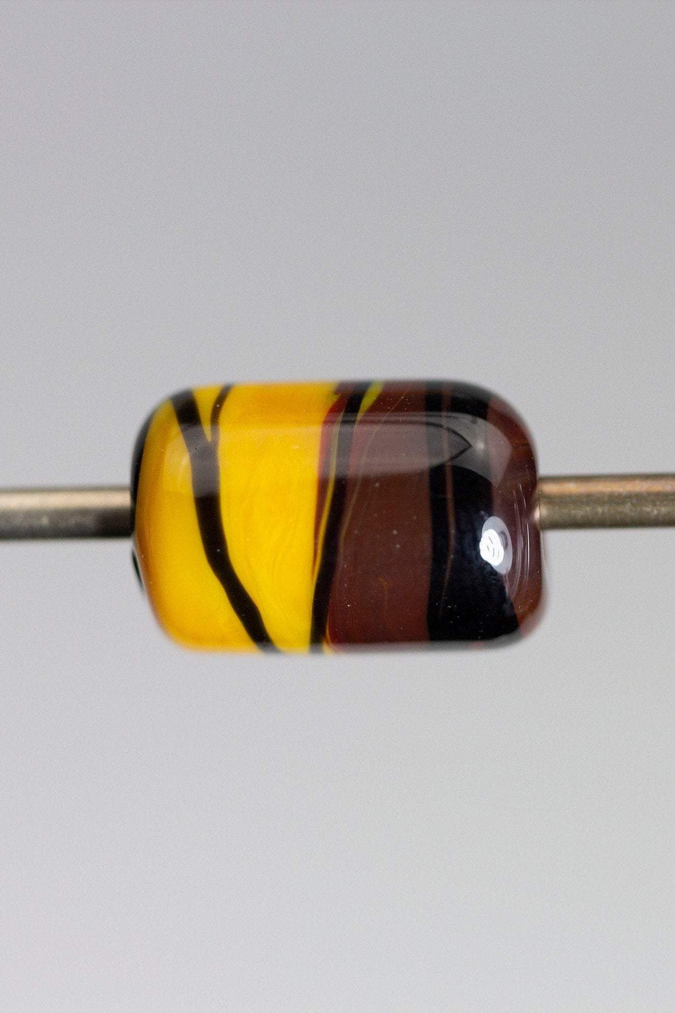 a handmade lampworked glass bead with black stripe on a yellow and brown background