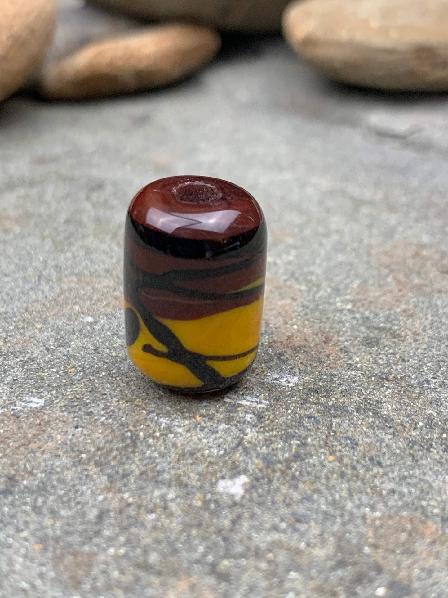 a handmade lampworked glass bead with black stripe on a yellow and brown background