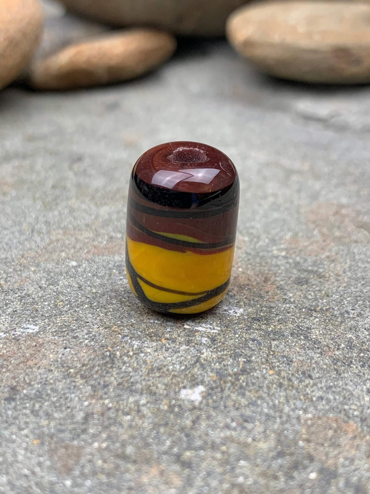 a handmade lampworked glass bead with black stripe on a yellow and brown background