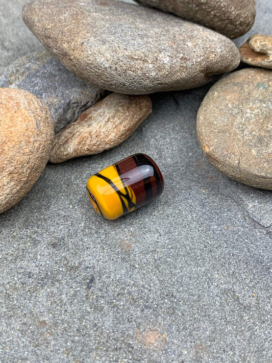a handmade lampworked glass bead with black stripe on a yellow and brown background