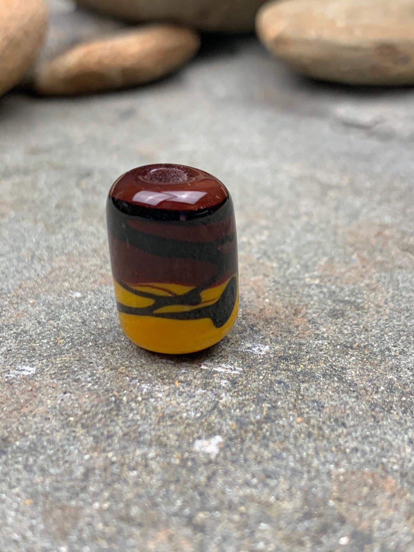 a handmade lampworked glass bead with black stripe on a yellow and brown background