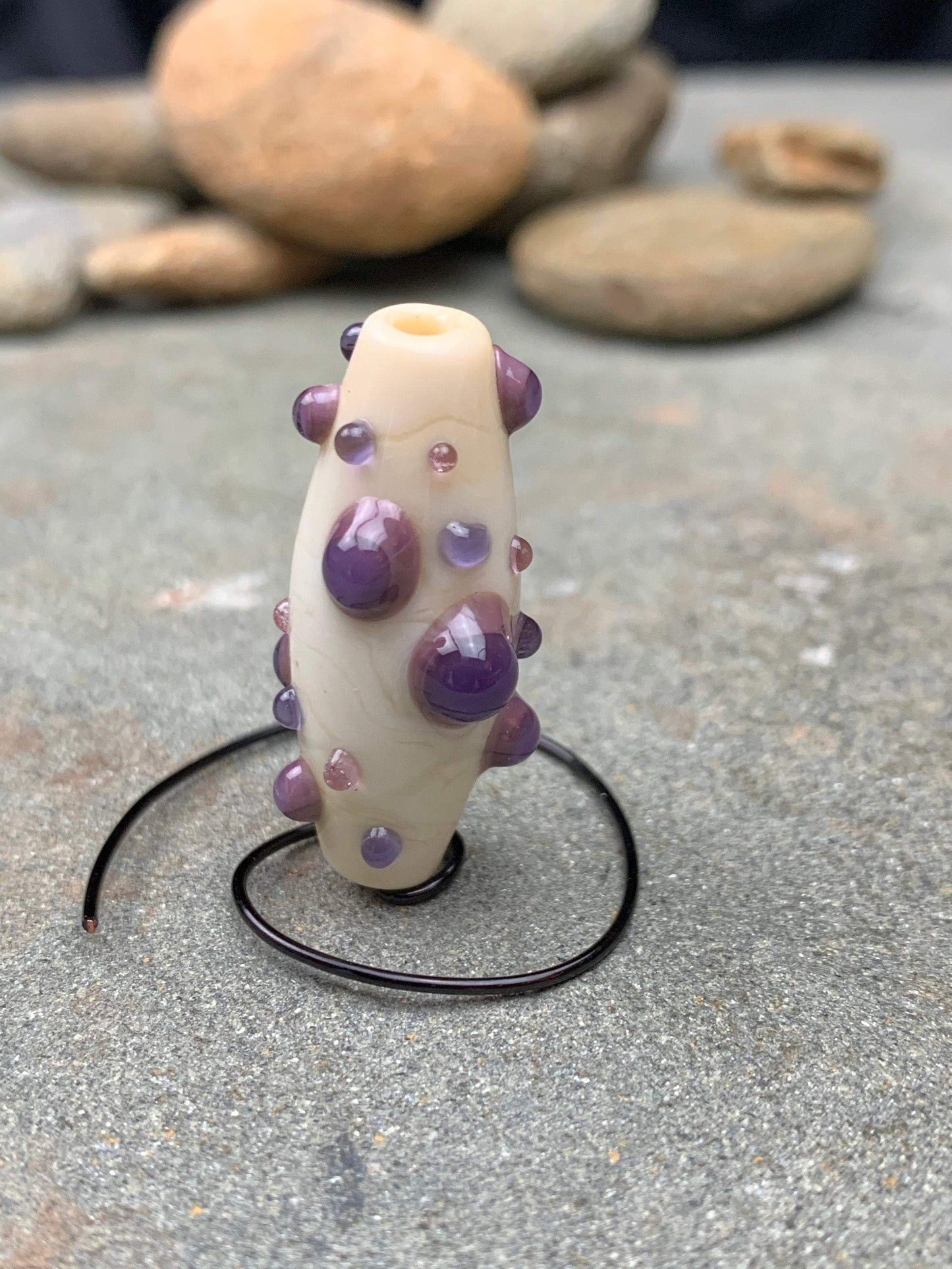 a handmade lampworked glass bead with purple and mauve dots on a white background