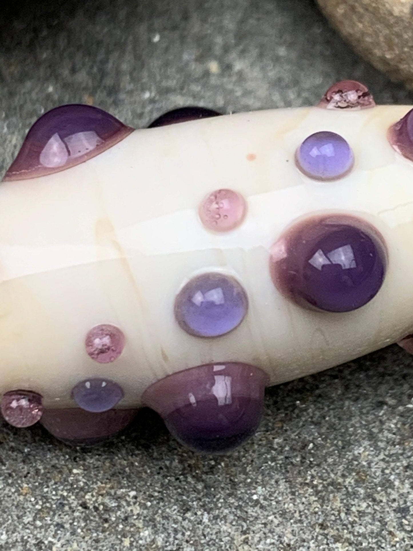a handmade lampworked glass bead with purple and mauve dots on a white background