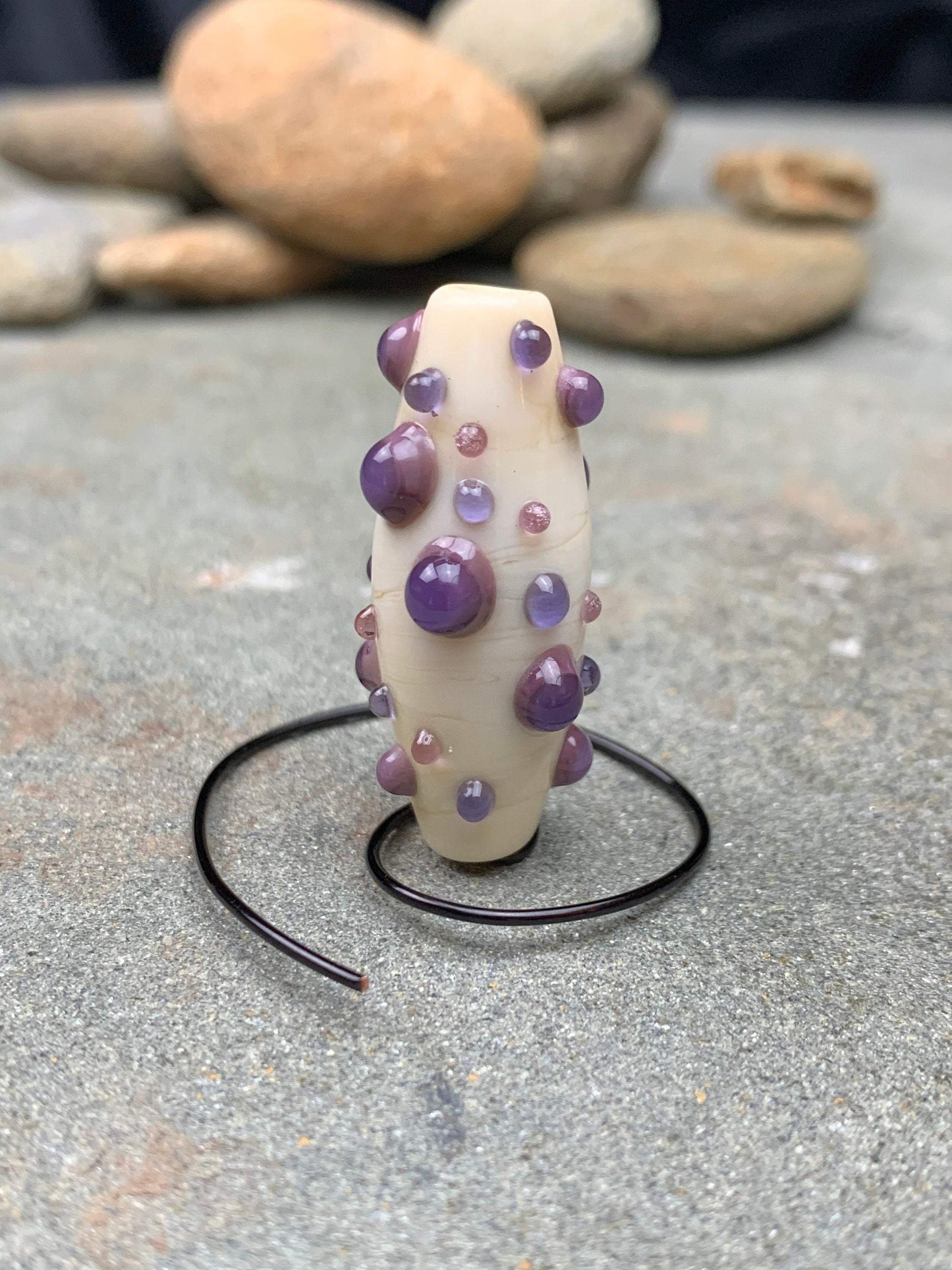a handmade lampworked glass bead with purple and mauve dots on a white background