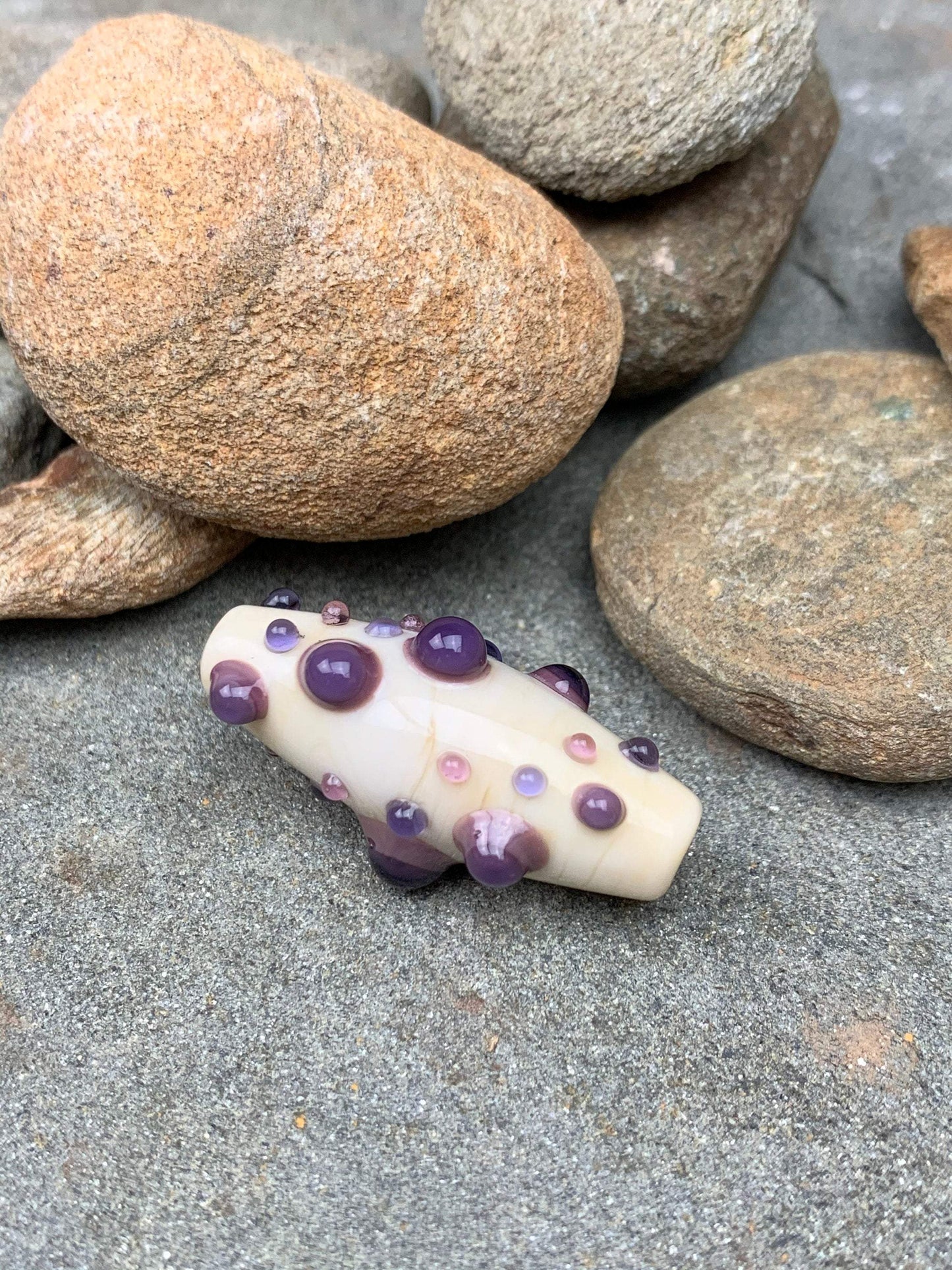 a handmade lampworked glass bead with purple and mauve dots on a white background