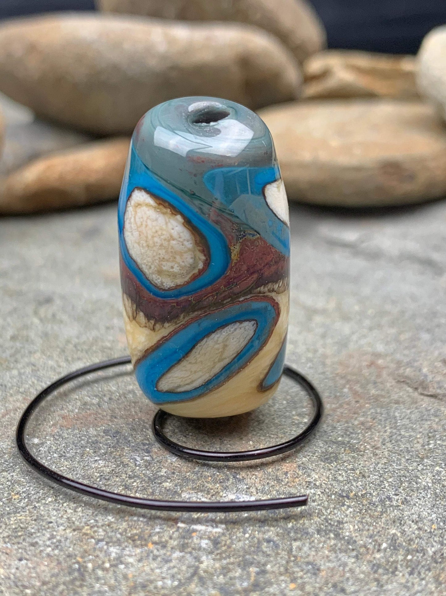 a handmade lampworked glass bead with turquoise and white dots on an ivory and brown background