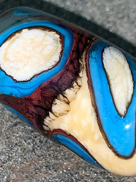 a handmade lampworked glass bead with turquoise and white dots on an ivory and brown background