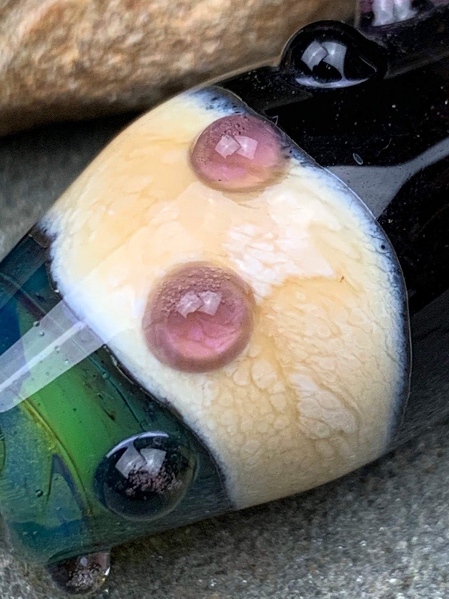 a handmade lampworked glass bead with pink dots on a teal, black and green background