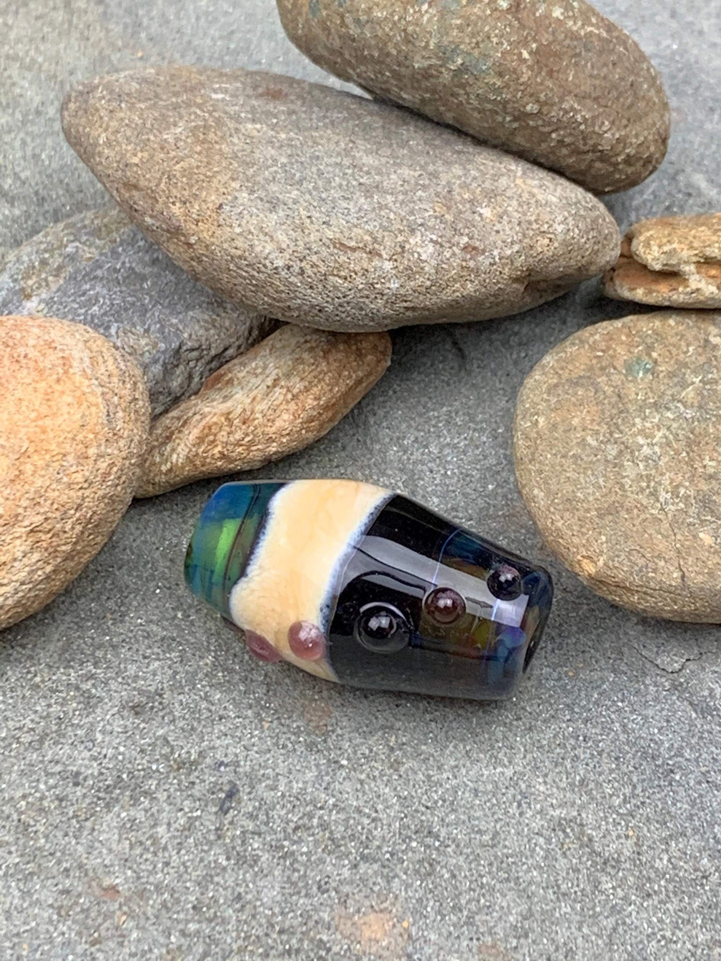 a handmade lampworked glass bead with pink dots on a teal, black and green background