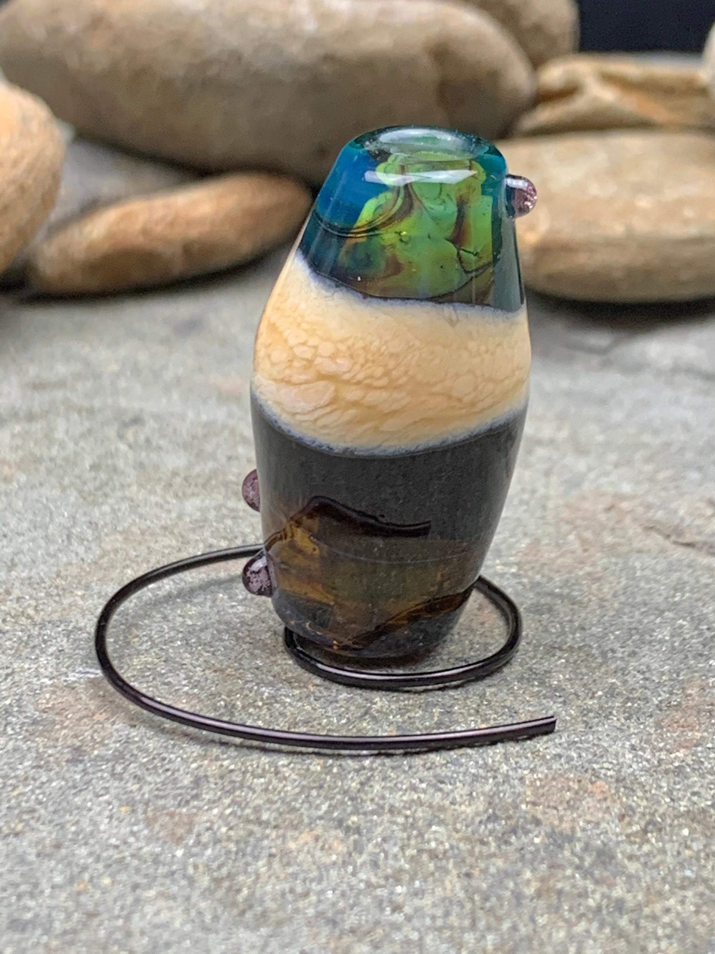 a handmade lampworked glass bead with pink dots on a teal, black and green background