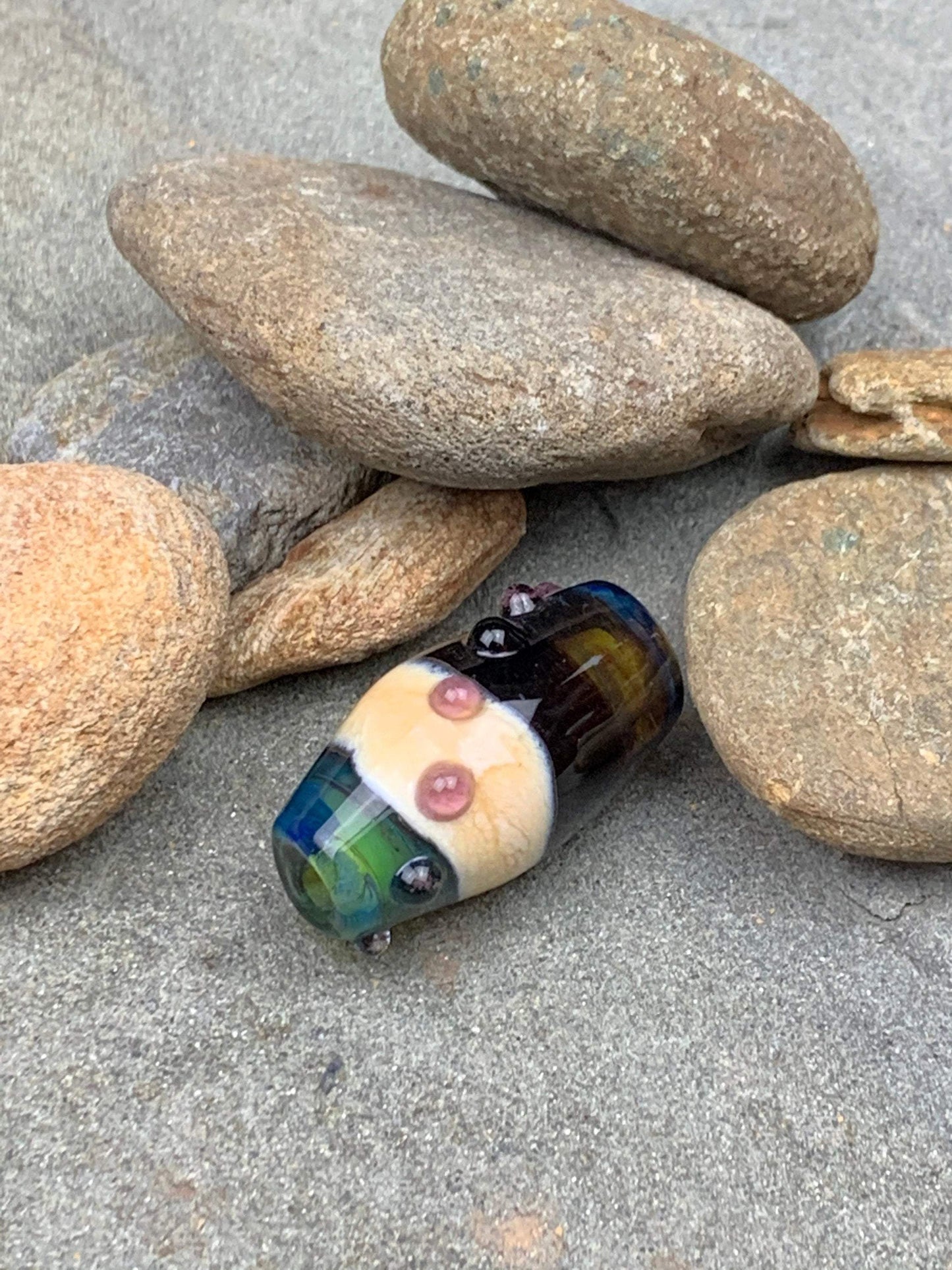 a handmade lampworked glass bead with pink dots on a teal, black and green background