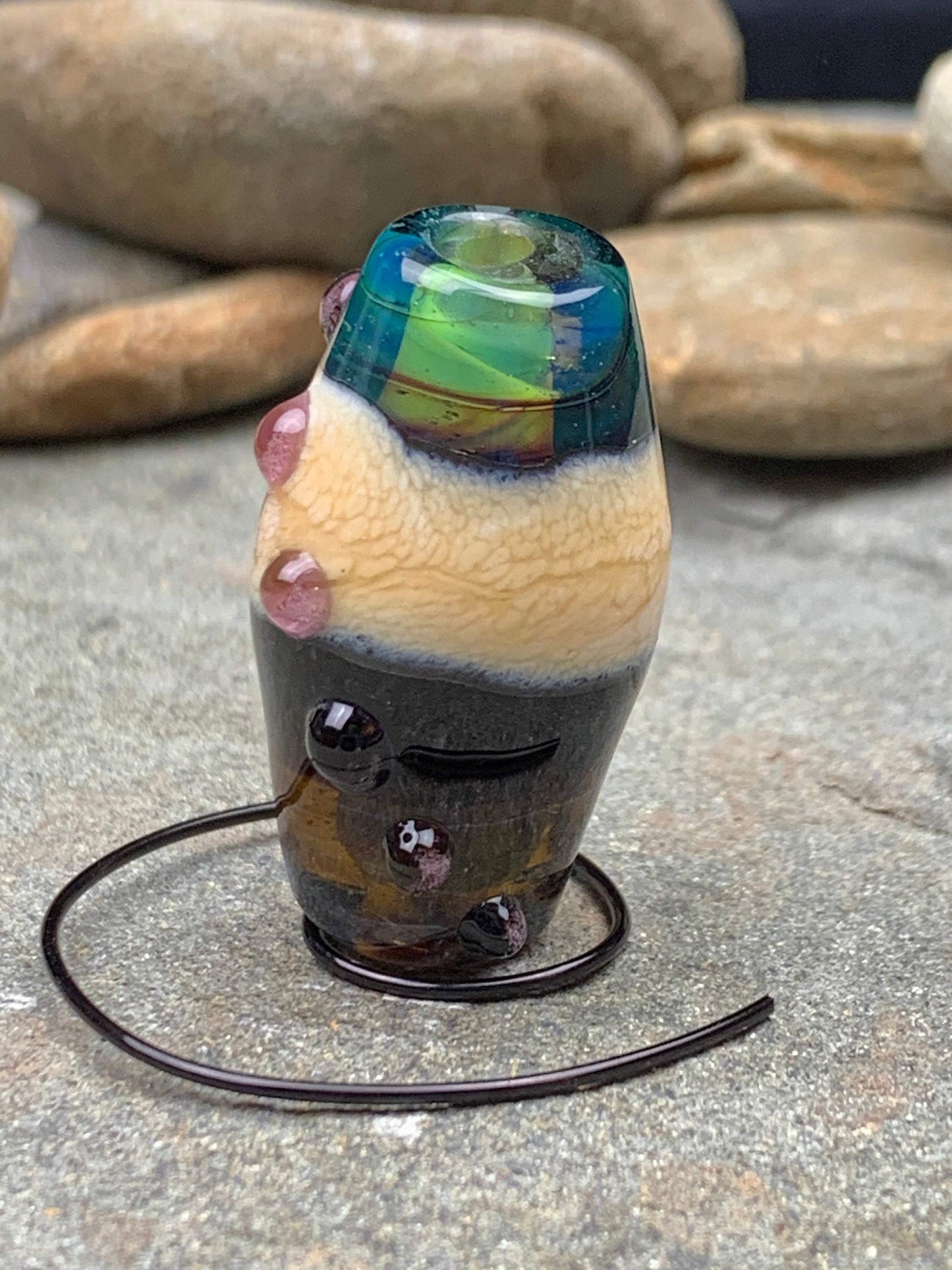 a handmade lampworked glass bead with pink dots on a teal, black and green background