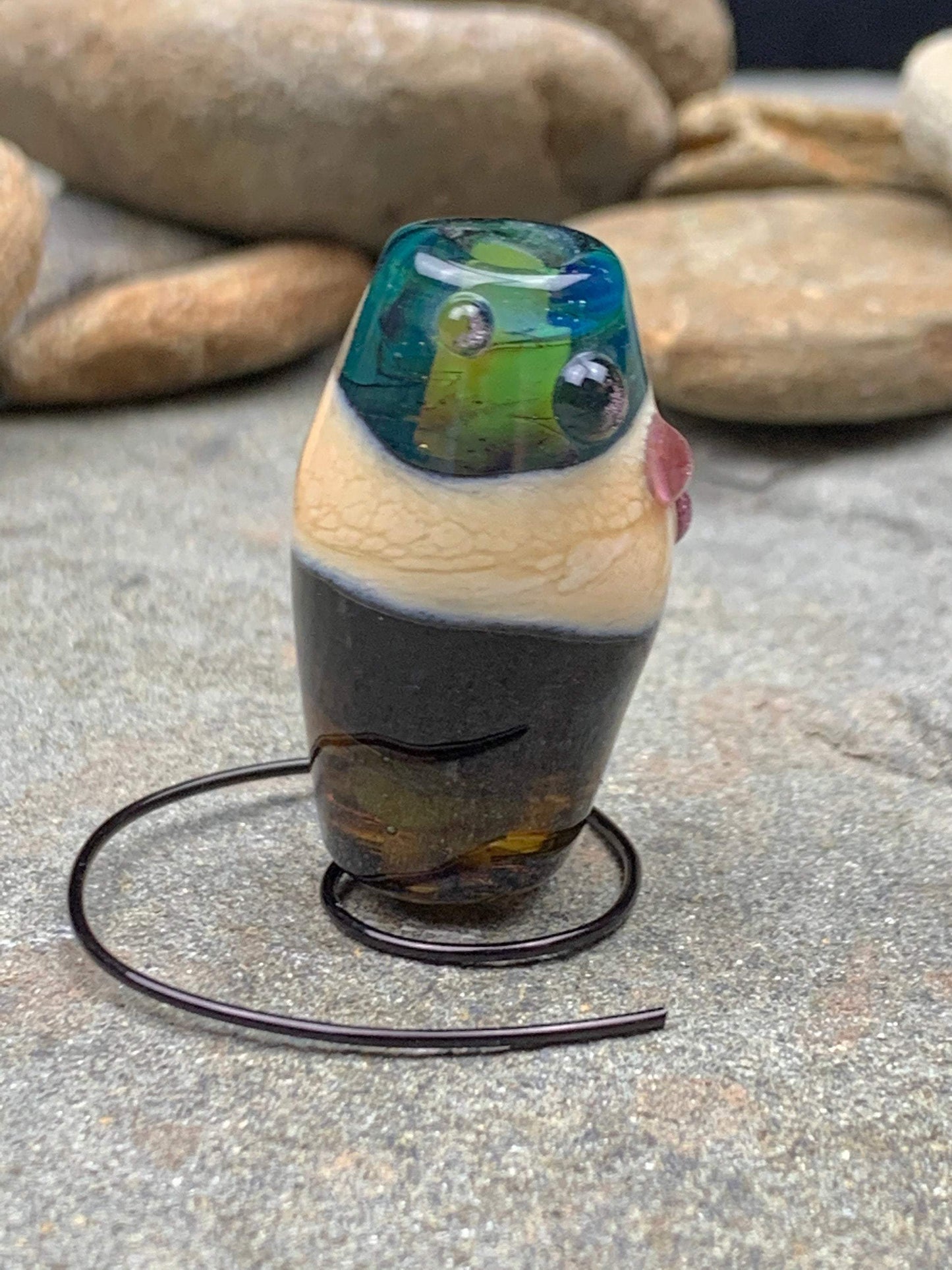 a handmade lampworked glass bead with pink dots on a teal, black and green background