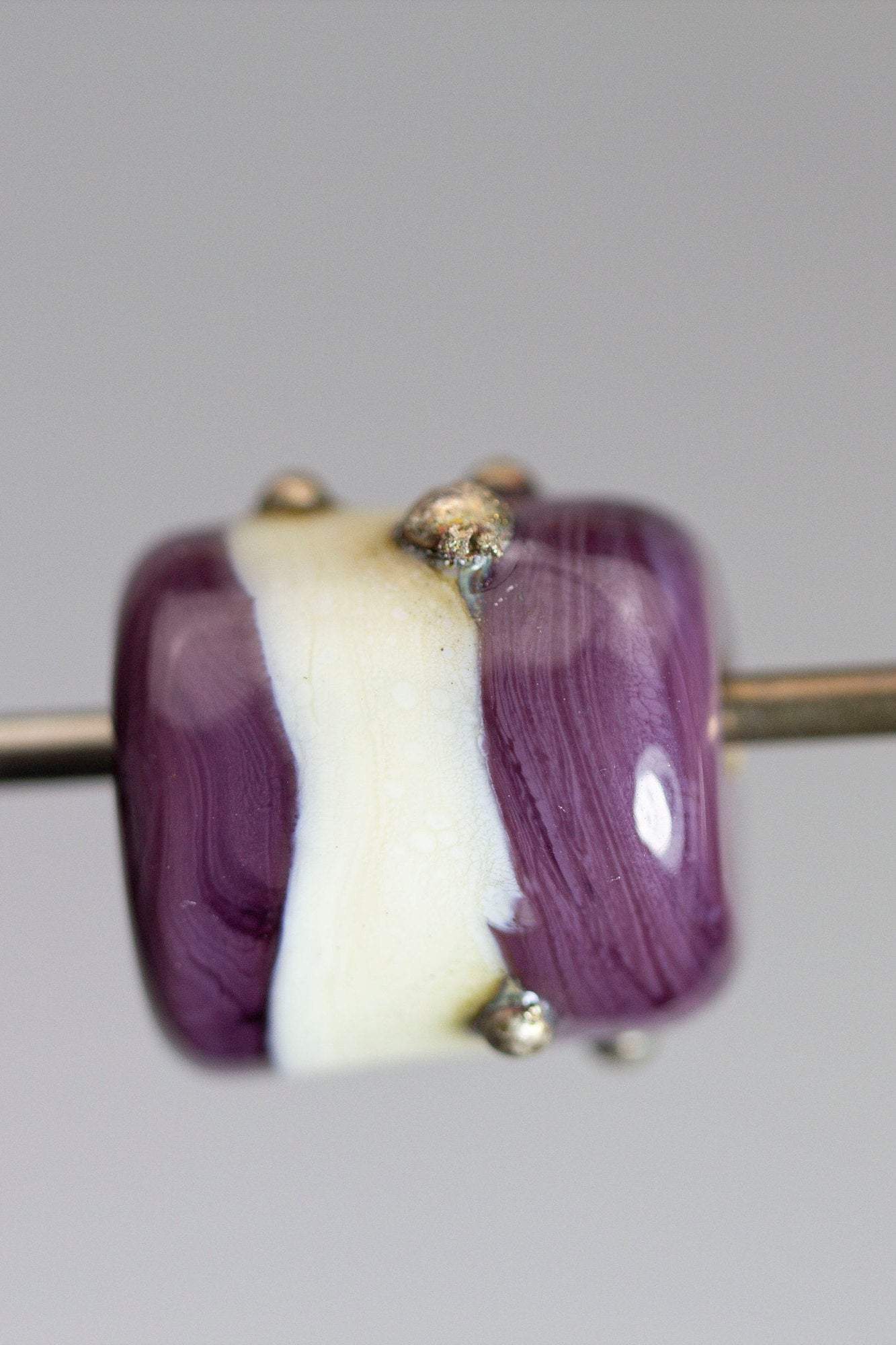 a handmade lampworked glass bead with real silver dots on an ivory and purple background