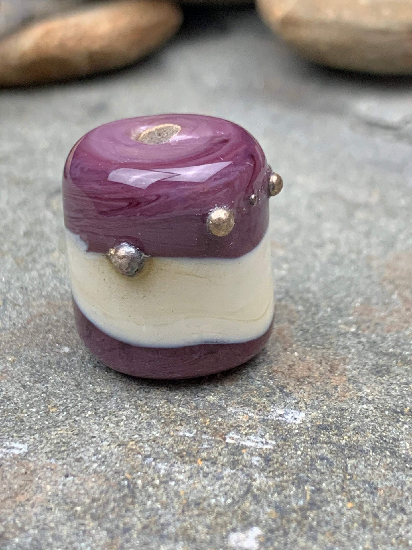 a handmade lampworked glass bead with real silver dots on an ivory and purple background