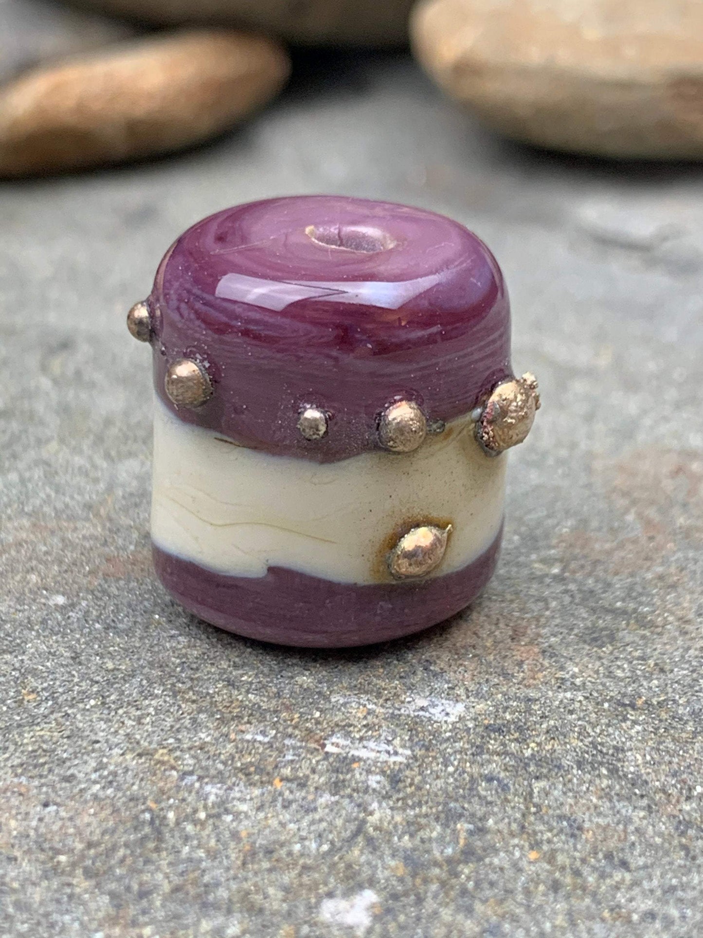 a handmade lampworked glass bead with real silver dots on an ivory and purple background