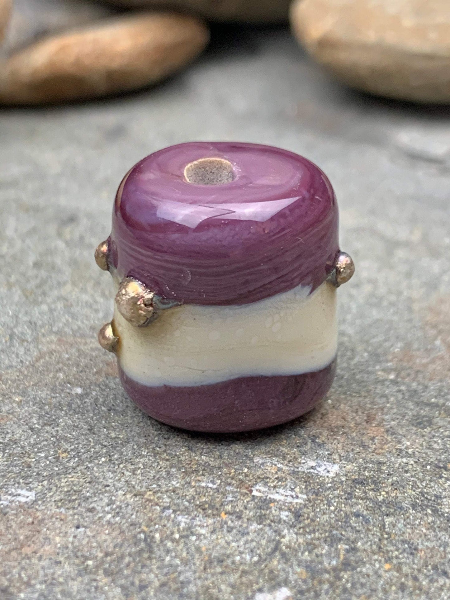 a handmade lampworked glass bead with real silver dots on an ivory and purple background