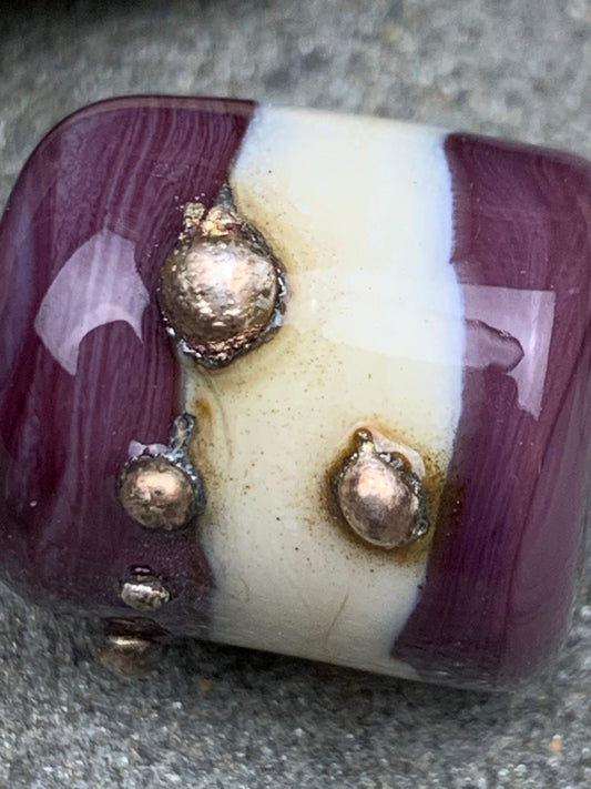 a handmade lampworked glass bead with real silver dots on an ivory and purple background