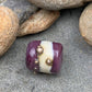 a handmade lampworked glass bead with real silver dots on an ivory and purple background