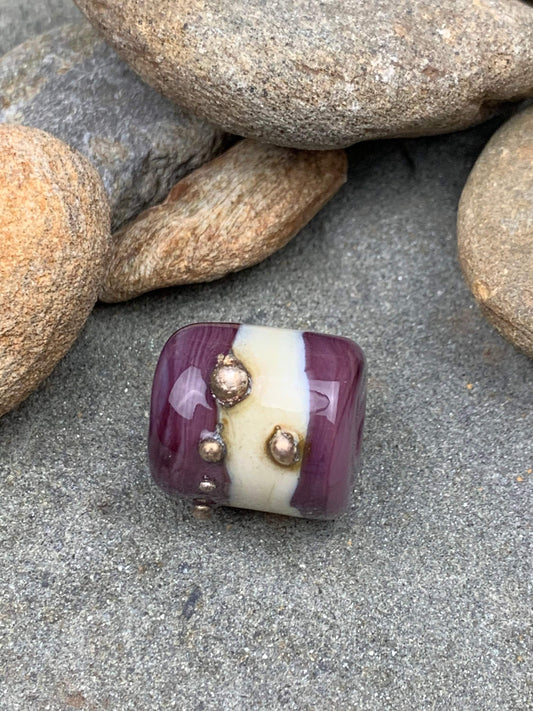 a handmade lampworked glass bead with real silver dots on an ivory and purple background