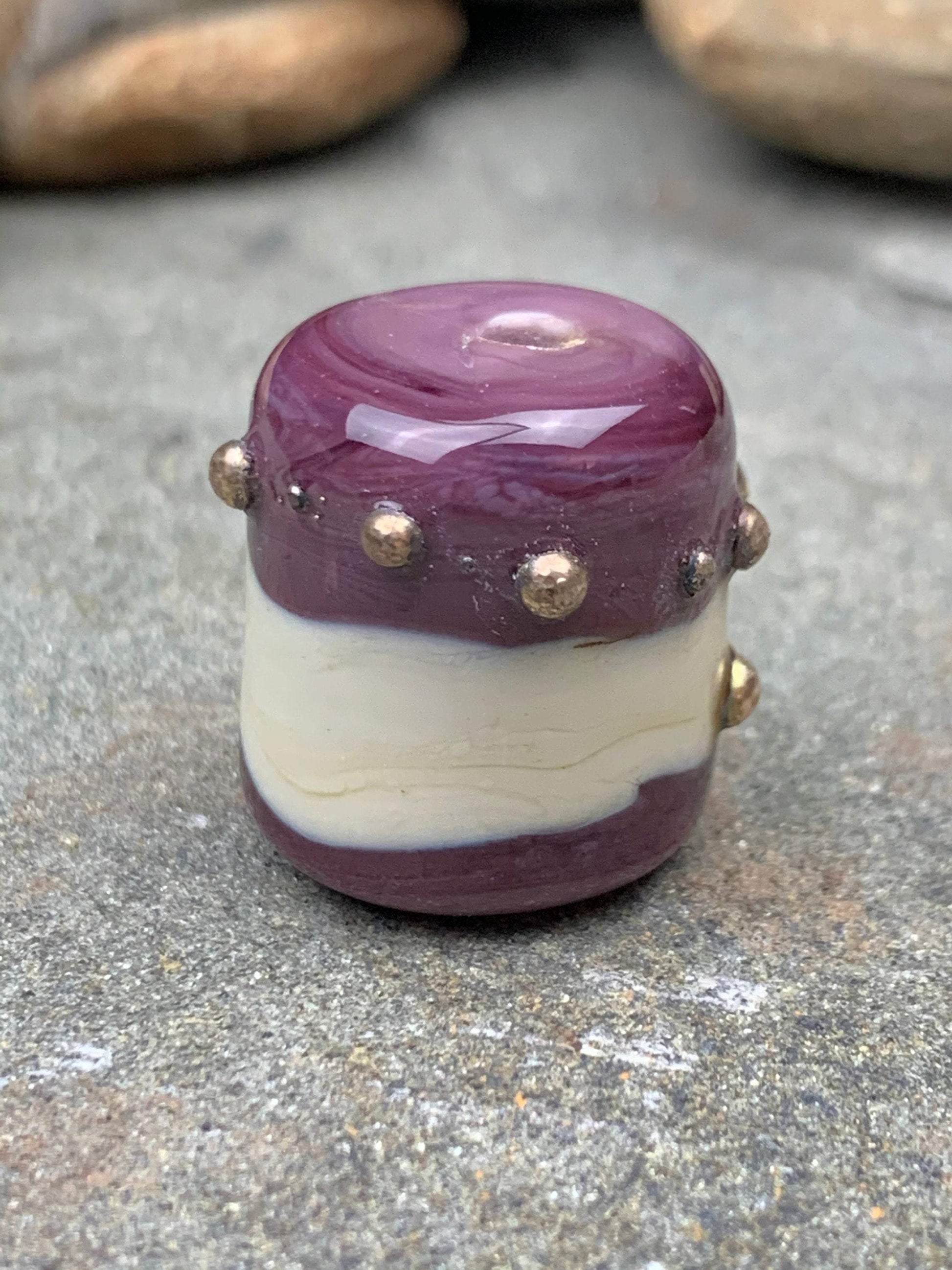 a handmade lampworked glass bead with real silver dots on an ivory and purple background