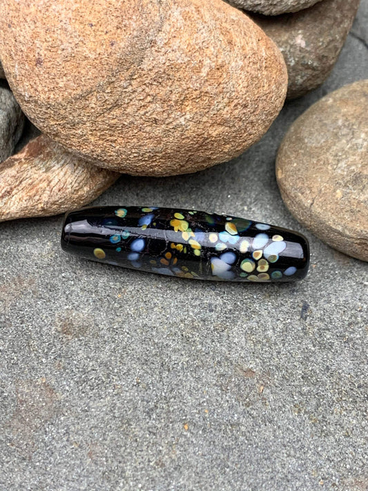 a handmade lampworked glass bead with multicolor dots on a black background