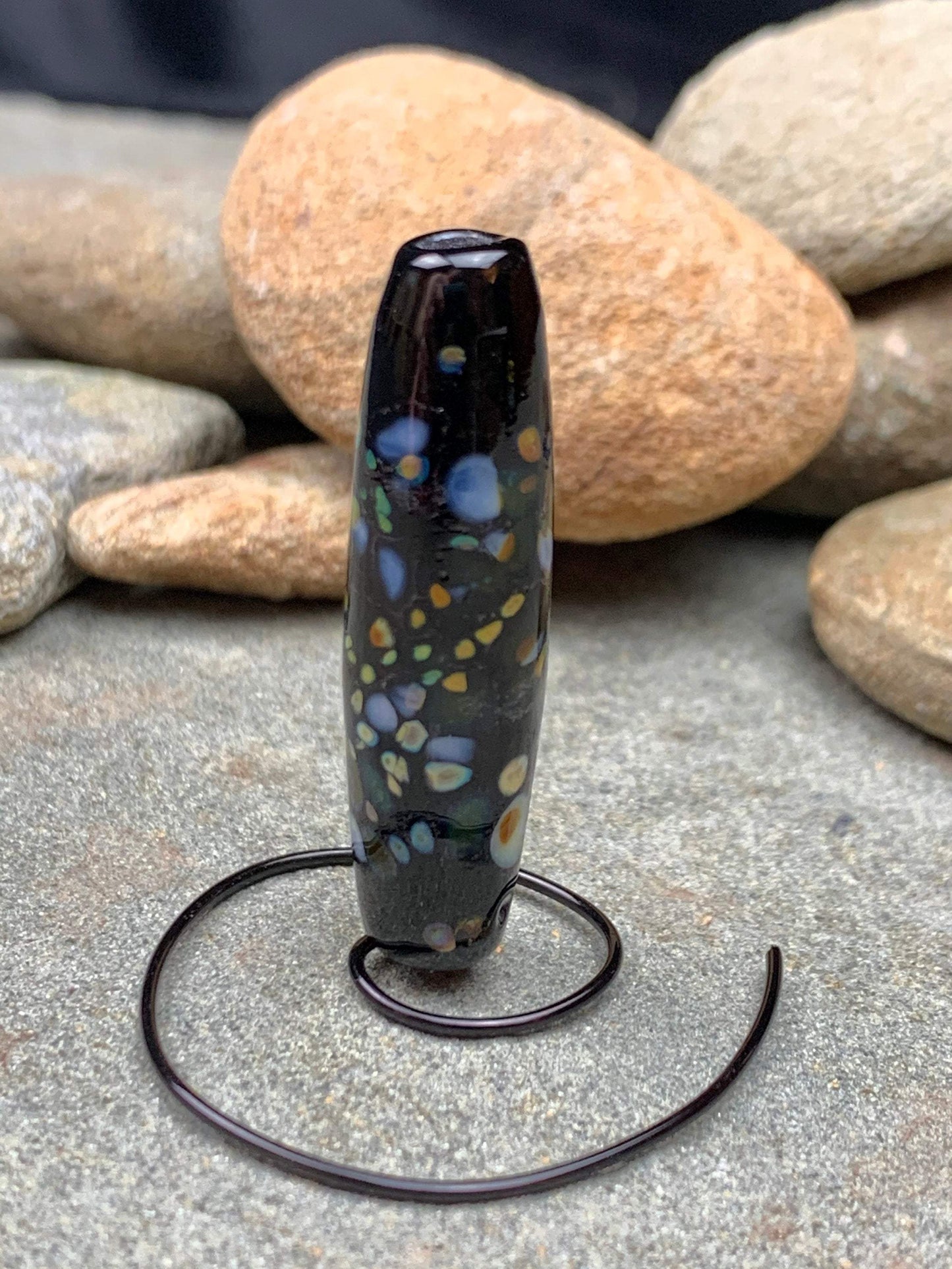 a handmade lampworked glass bead with multicolor dots on a black background