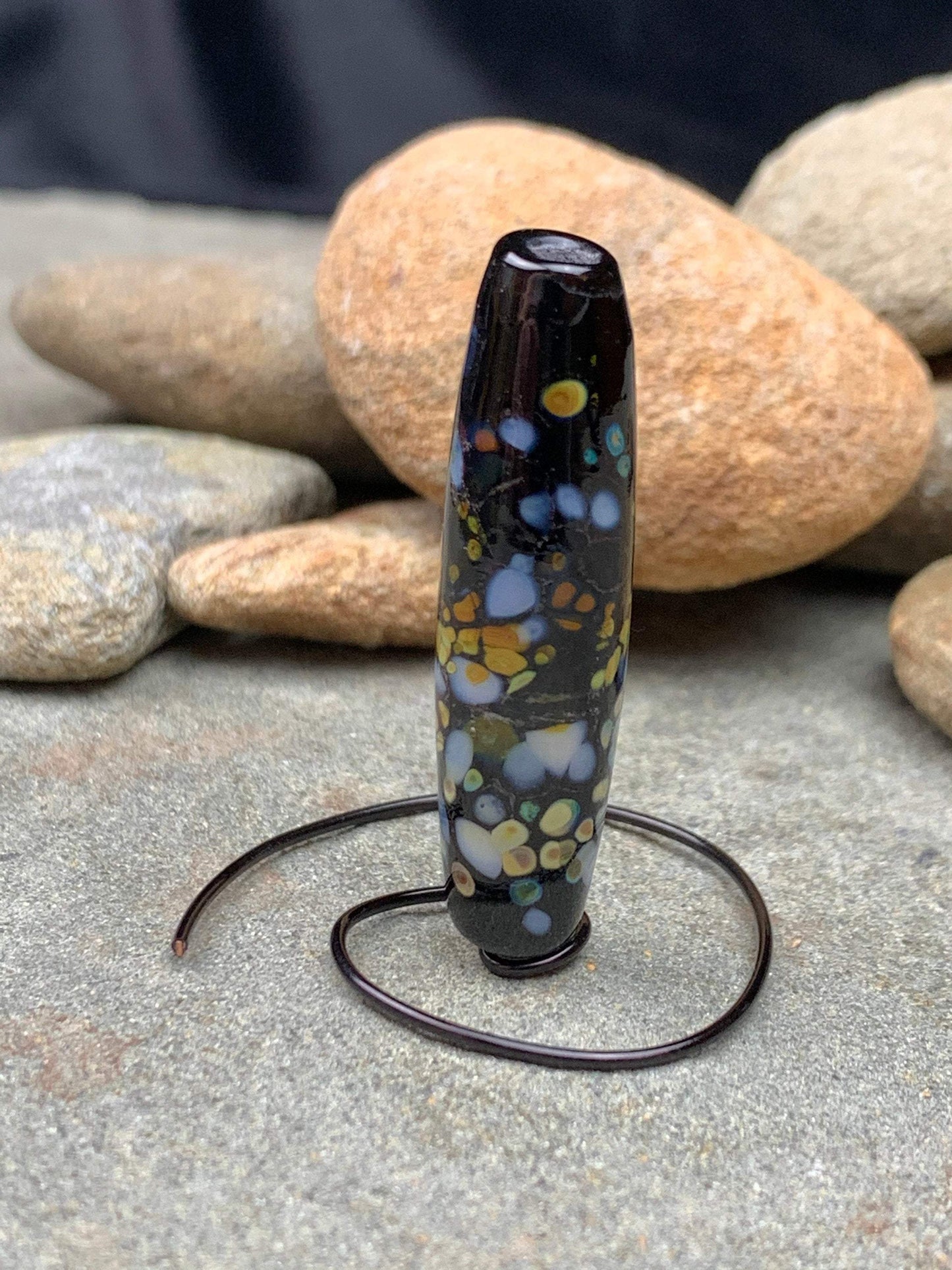 a handmade lampworked glass bead with multicolor dots on a black background