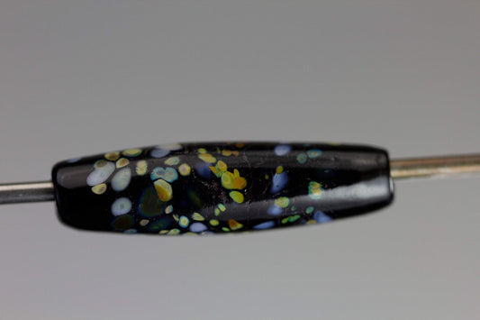 a handmade lampworked glass bead with multicolor dots on a black background