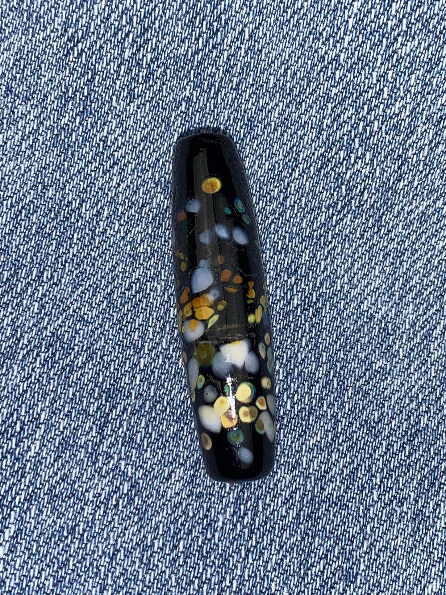 a handmade lampworked glass bead with multicolor dots on a black background