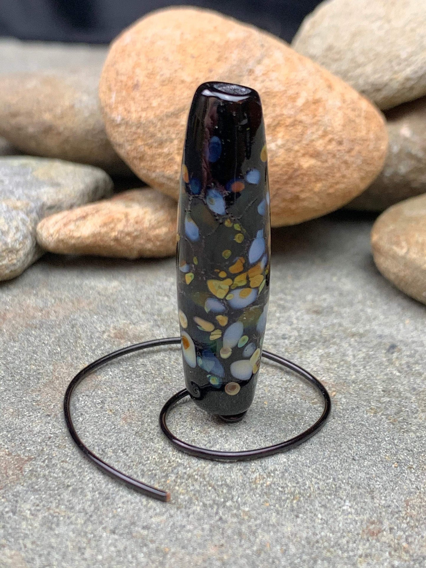 a handmade lampworked glass bead with multicolor dots on a black background