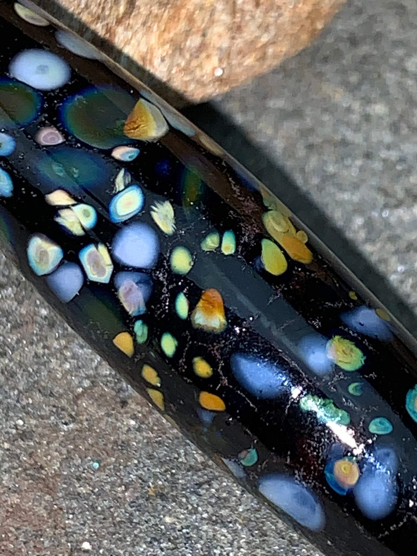 a handmade lampworked glass bead with multicolor dots on a black background