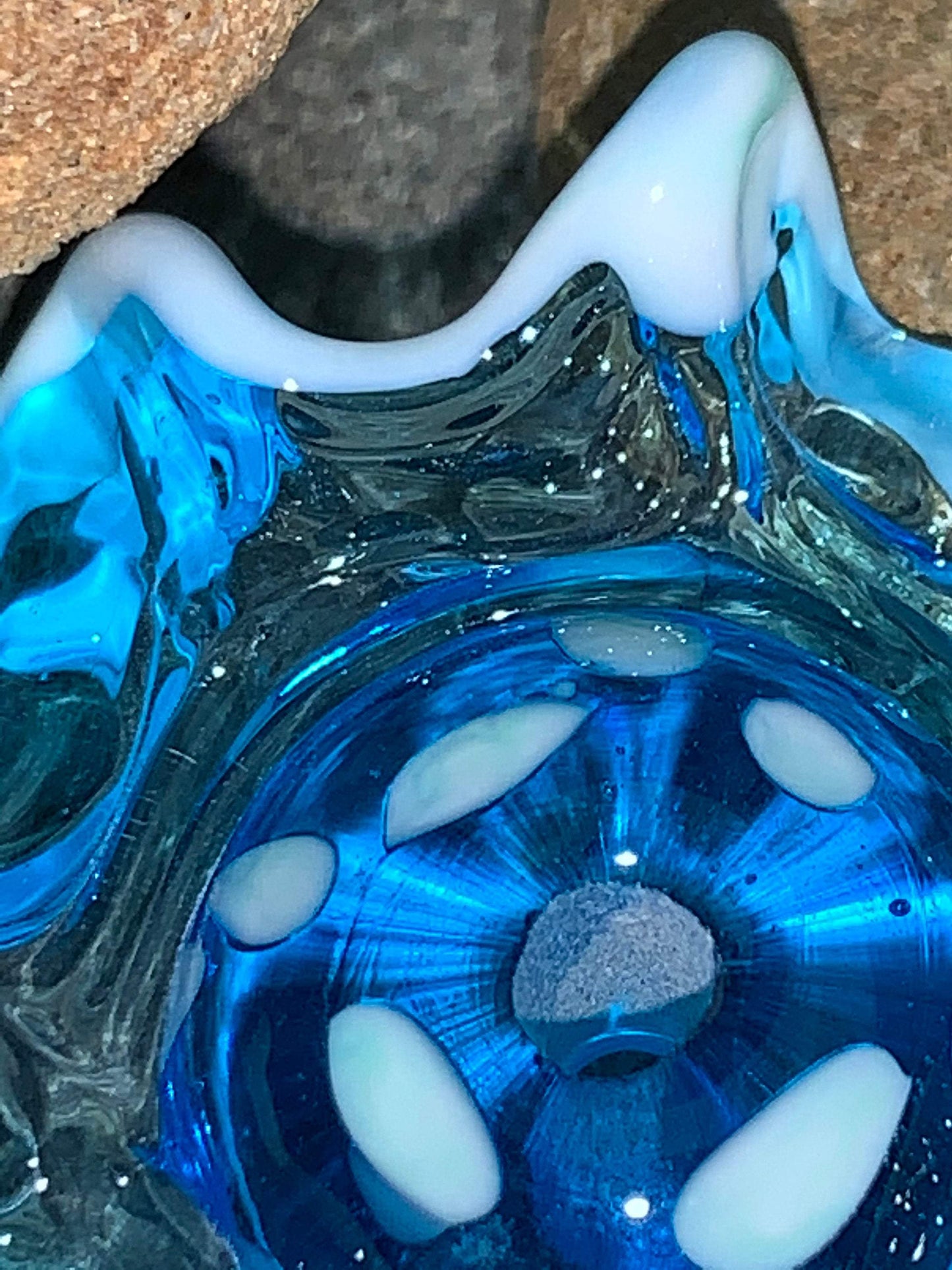 a handmade lampworked blue glass bead with a blue glass ruffle with white dots around the middle of the bead.