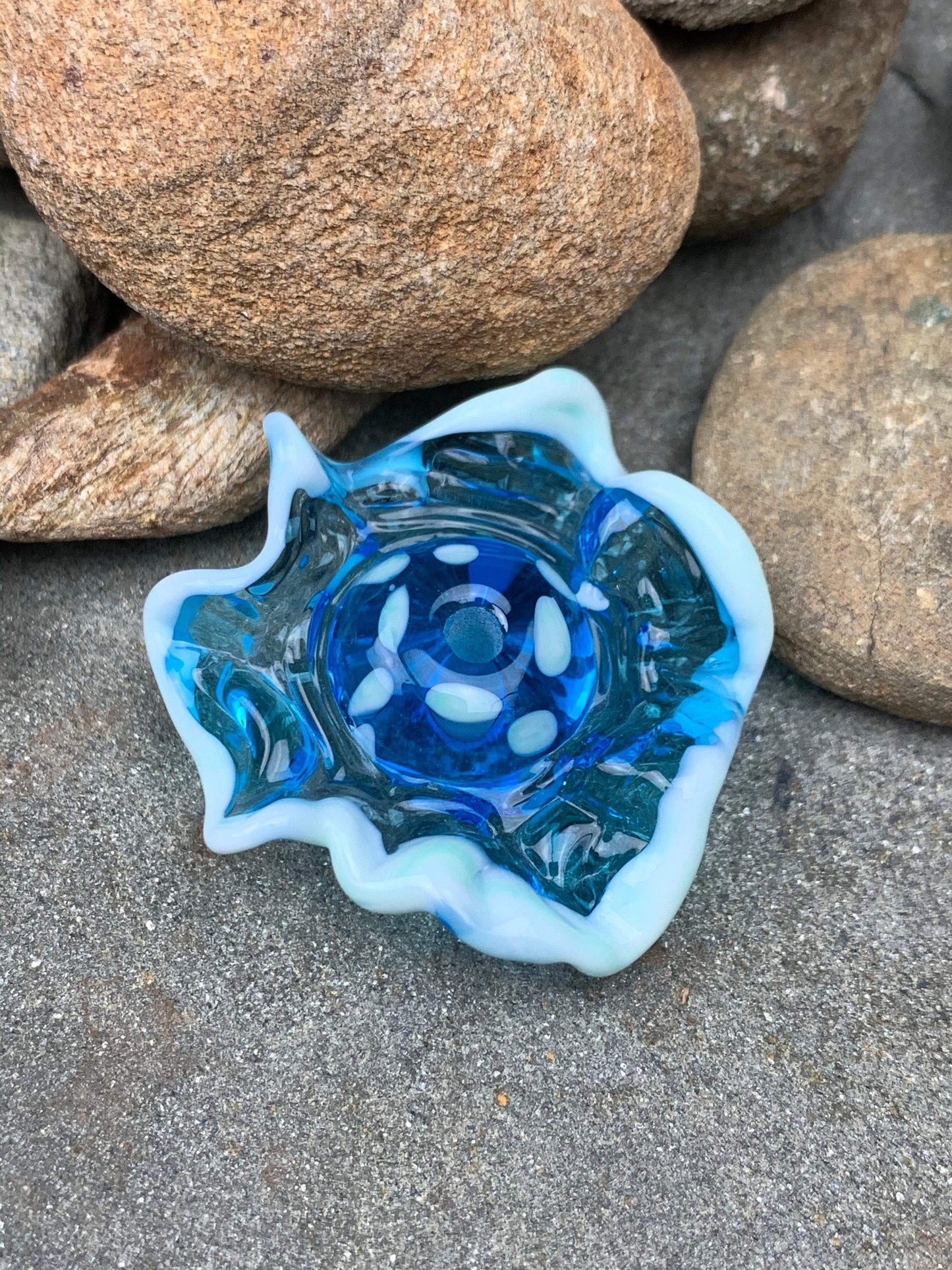 a handmade lampworked blue glass bead with a blue glass ruffle with white dots around the middle of the bead.