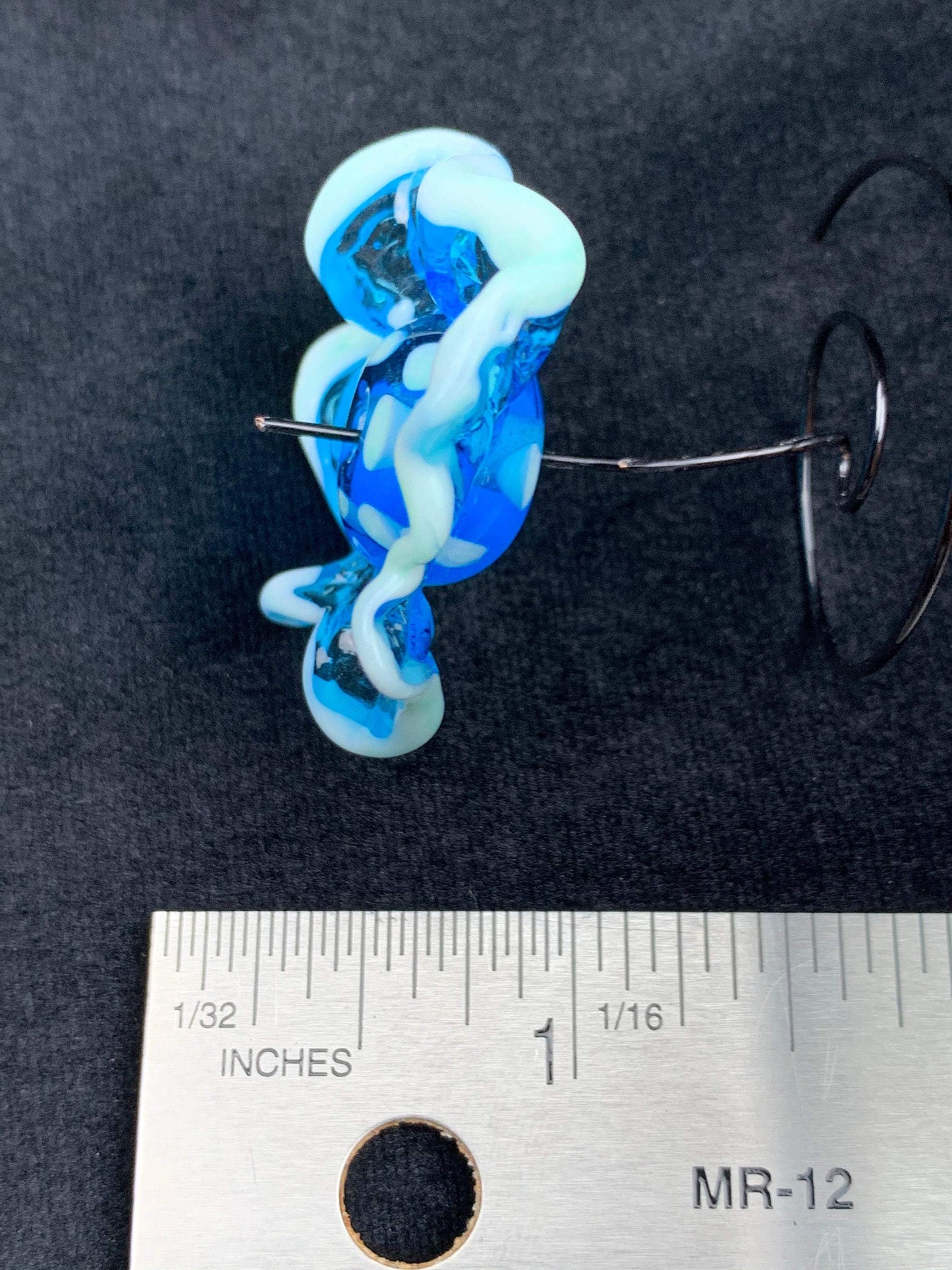a handmade lampworked blue glass bead with a blue glass ruffle with white dots around the middle of the bead.