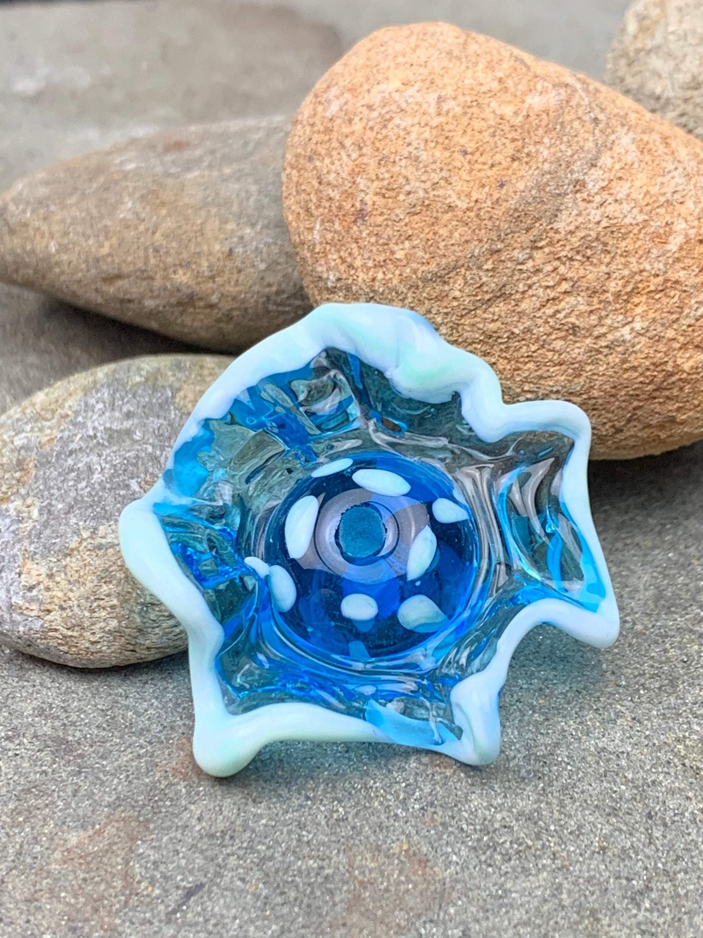 a handmade lampworked blue glass bead with a blue glass ruffle with white dots around the middle of the bead.