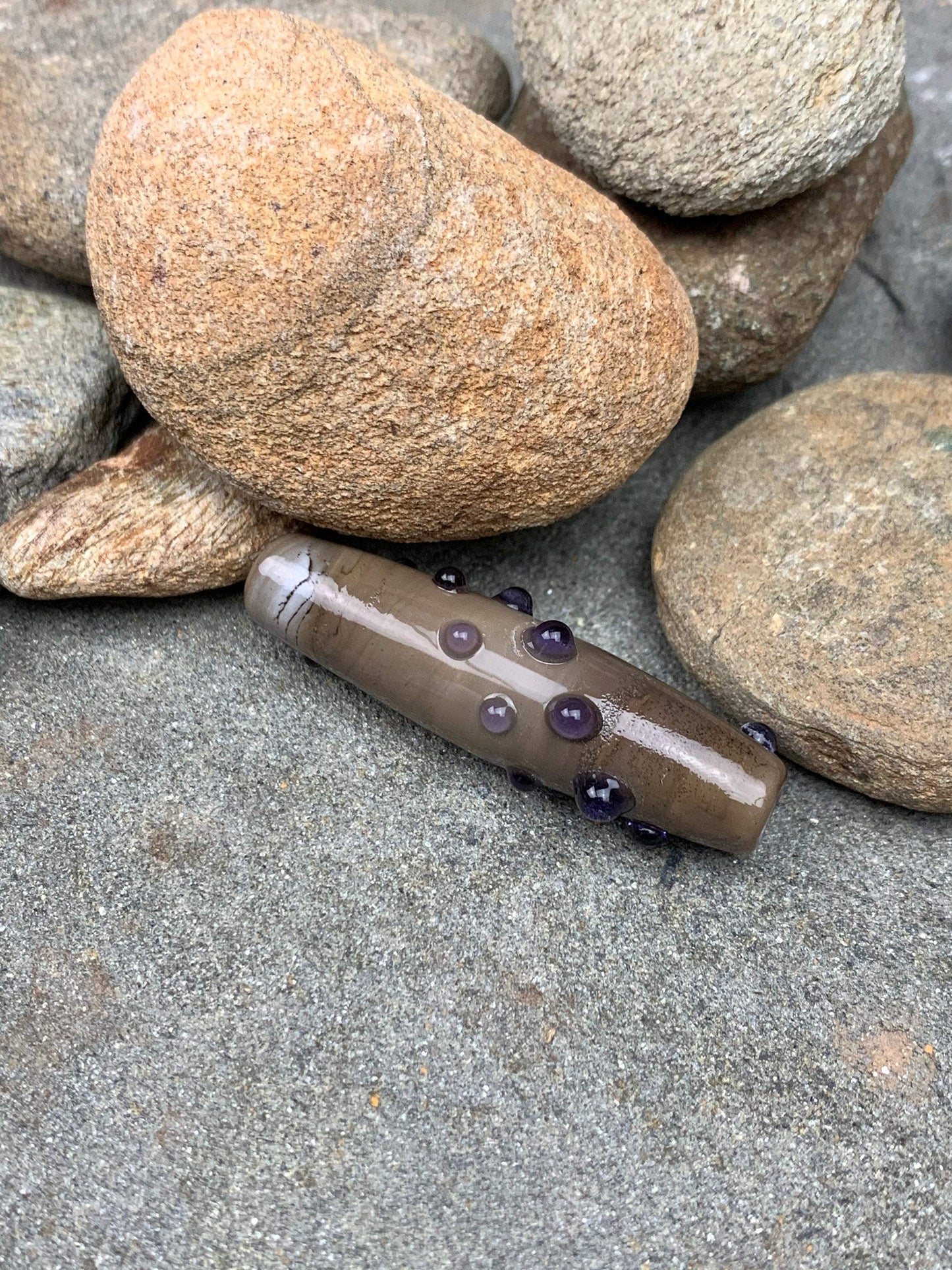 a handmade lampworked glass bead with purple dots on sage gray background