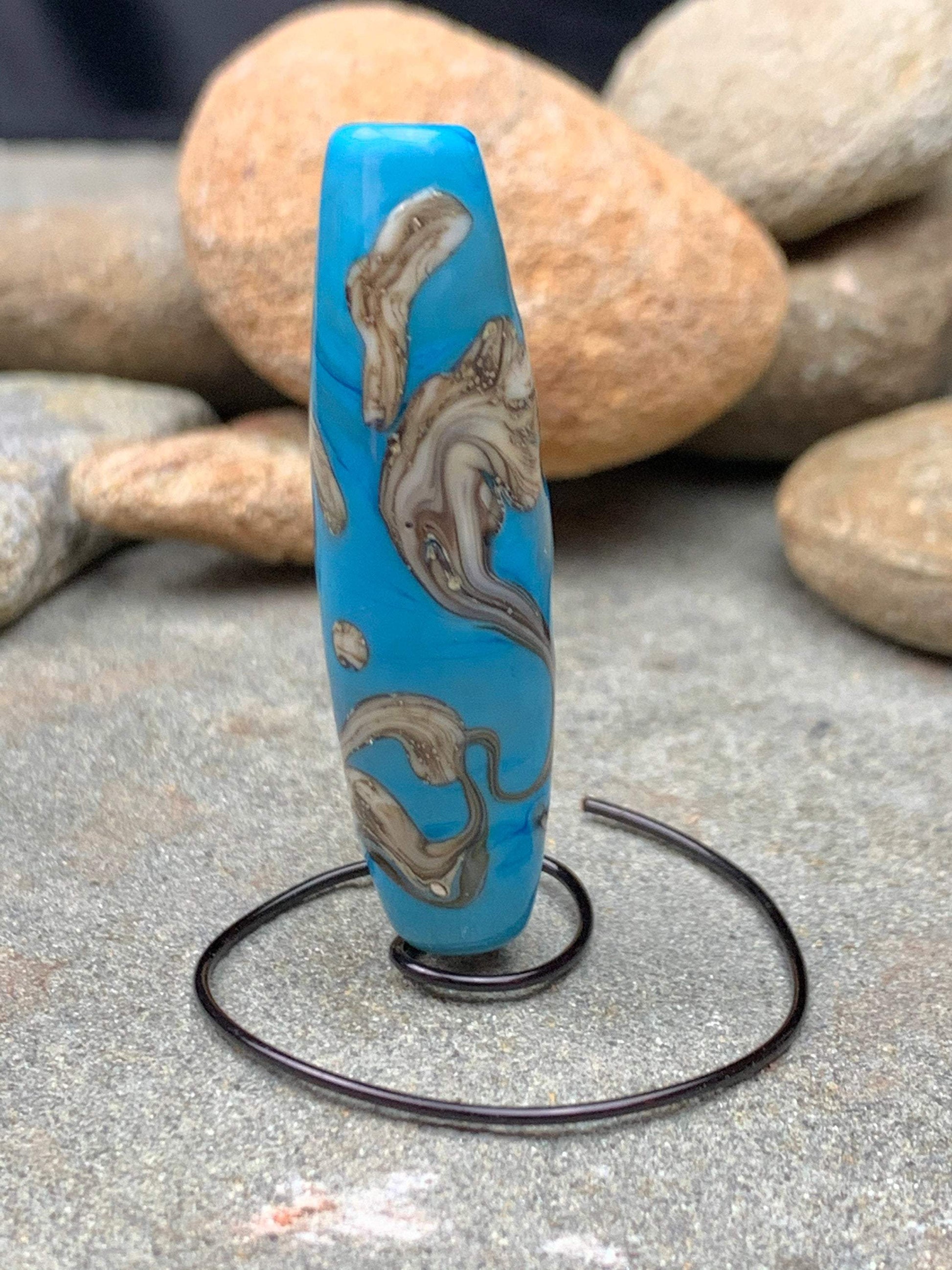 a handmade lampworked glass bead with silver and ivory swirls on a turquoise background
