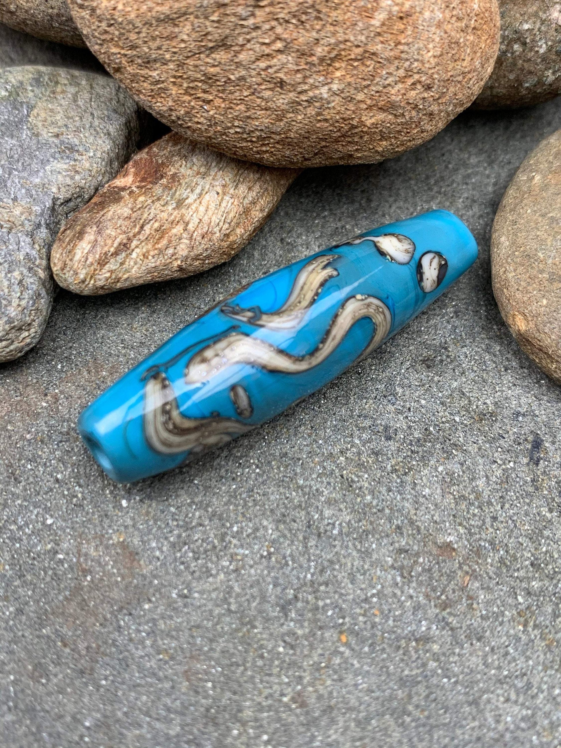 a handmade lampworked glass bead with silver and ivory swirls on a turquoise background