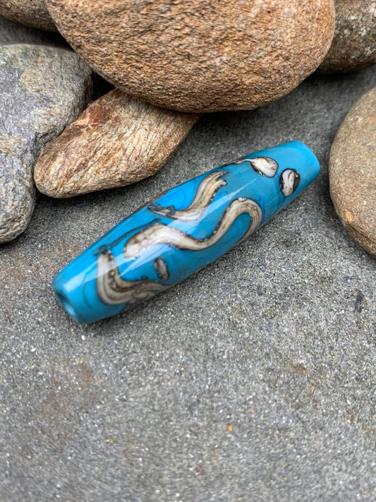 a handmade lampworked glass bead with silver and ivory swirls on a turquoise background