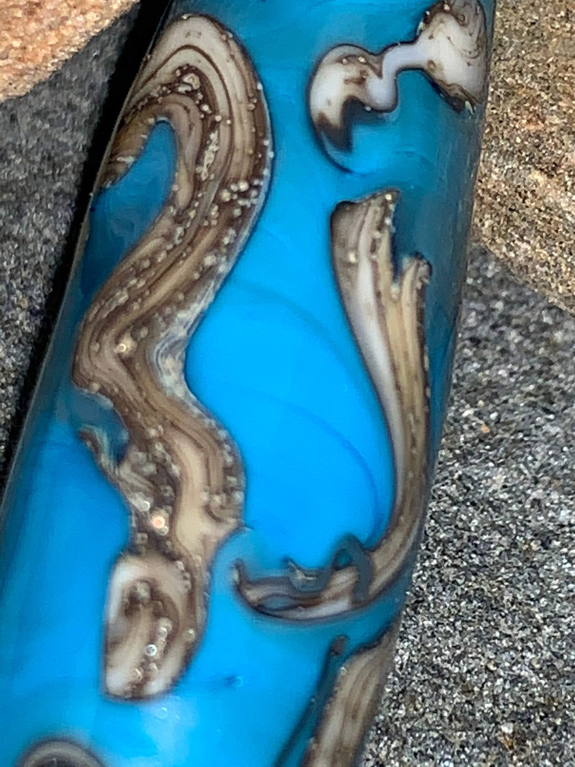 a handmade lampworked glass bead with silver and ivory swirls on a turquoise background