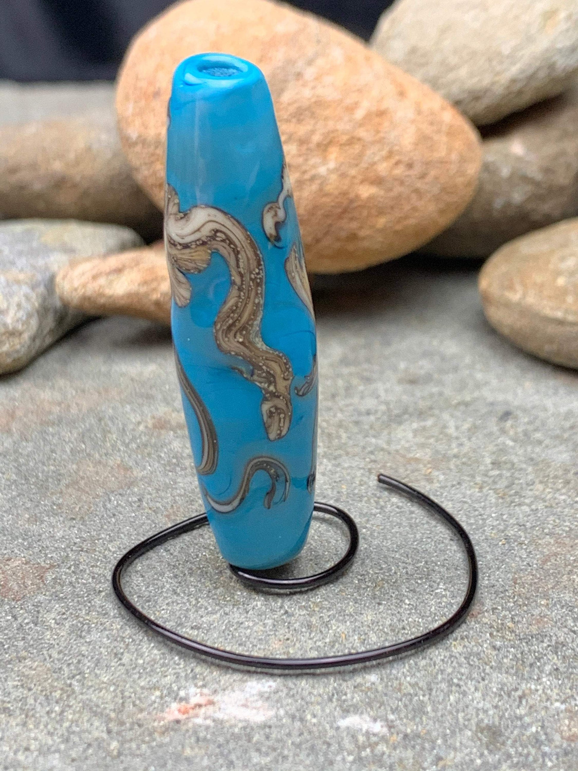 a handmade lampworked glass bead with silver and ivory swirls on a turquoise background