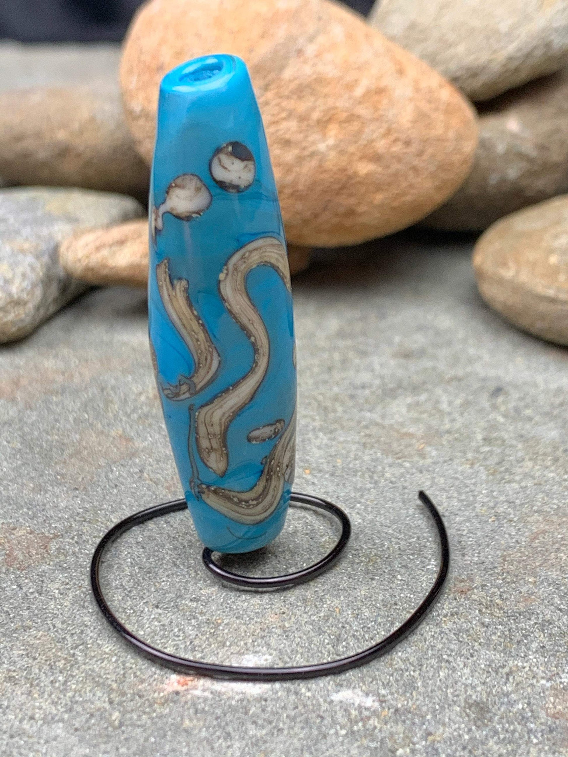 a handmade lampworked glass bead with silver and ivory swirls on a turquoise background