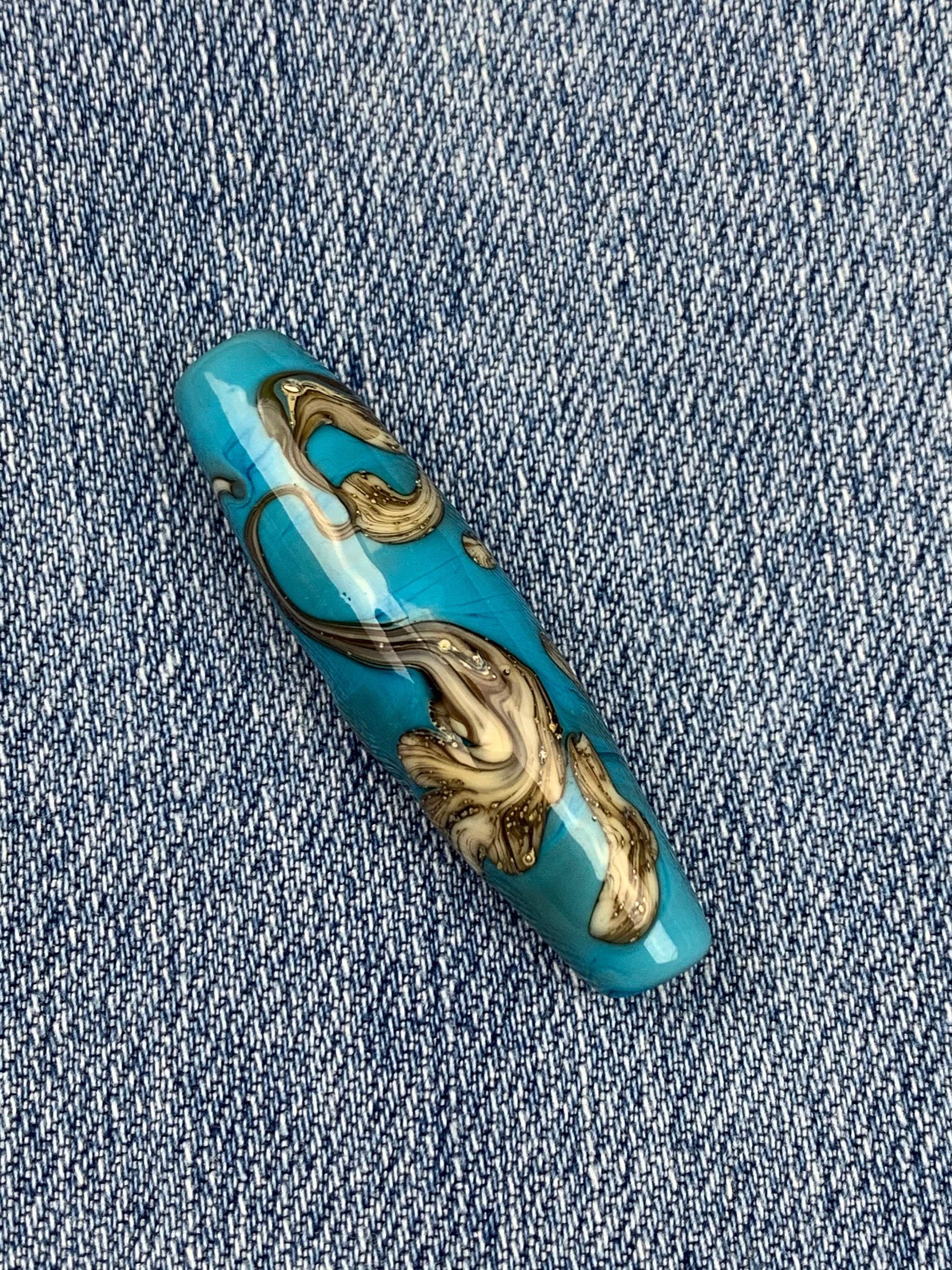 a handmade lampworked glass bead with silver and ivory swirls on a turquoise background