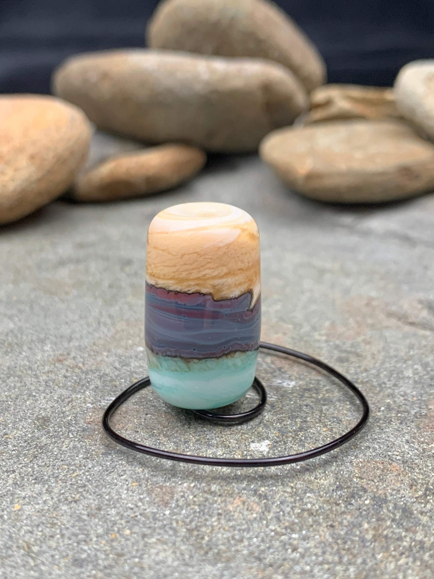 a handmade lampworked glass bead made of ivory, purple, and turquoise glass swirled into bands.