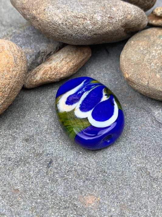 a handmade lampworked glass bead with blue and white dots on a green background